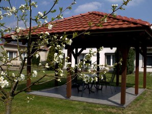 A gazebo with a tiled roof, surrounded by a grassy area and blooming trees. - Holiday Home With 1 Bedroom (Unterspreewald)