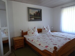 A bedroom with a wooden bed, two nightstands, a mirror, a painting on the wall, and a window with curtains. - Holiday Home With 1 Bedroom (Unterspreewald)