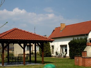 A residential area with a gazebo, a brick barbecue, and a house with a red-tiled roof. - Holiday Home With 1 Bedroom (Unterspreewald)