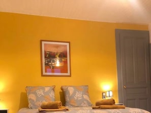 A hotel room with a bed, two pillows, a framed picture on the wall, a door, and a nightstand with a lamp. - Holiday Home in Trevigin With Wi-fi (Trevignin)