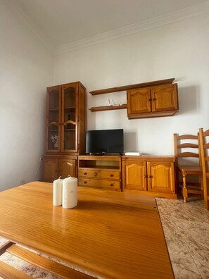 Ein Zimmer mit einem Holzesstisch, einem Fernseher auf einem Schrank, Holzschränken und einem Stuhl.