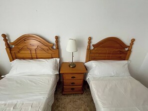 Un lit double avec une tête de lit en bois, une table de chevet avec une lampe et une petite commode en bois.