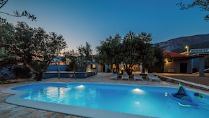 Une piscine aux bords recouverts de pierres, entourée de chaises longues et d’arbres.
