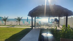 A beachside patio with a thatched umbrella, outdoor seating, and a view of the ocean. - 2 Bdrm unit ON VANDERBILT BEACH. Oct 24-31 (Naples)