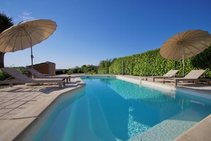 A swimming pool with lounge chairs and umbrellas, surrounded by a hedge and a building. - Villa Richemont - Panoramic Views & Private Pool (Brantôme en Périgord)