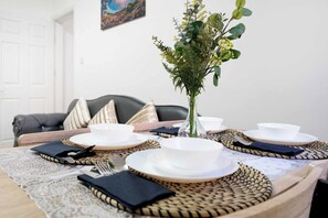 A dining table set with white plates, bowls, and cutlery, with a vase of greenery in the center. - Ground-Floor 2BR Newcastle Retreat | Sleeps 4 (Newcastle upon Tyne)