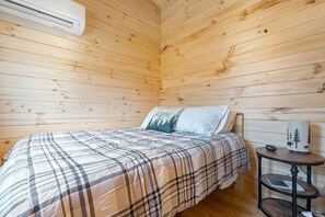 Une pièce aux murs lambrés, comprenant un lit, une table de chevet et un climatiseur fixé au mur.