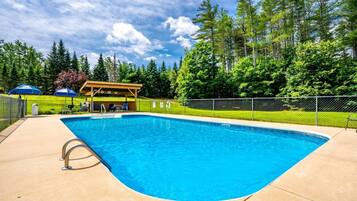Una piscina rectangular con una terraza de madera y un área de estar cubierta.