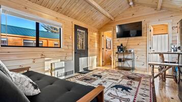 L’intérieur d’un chalet chaleureux, avec un canapé, un téléviseur et un plafond en bois.
