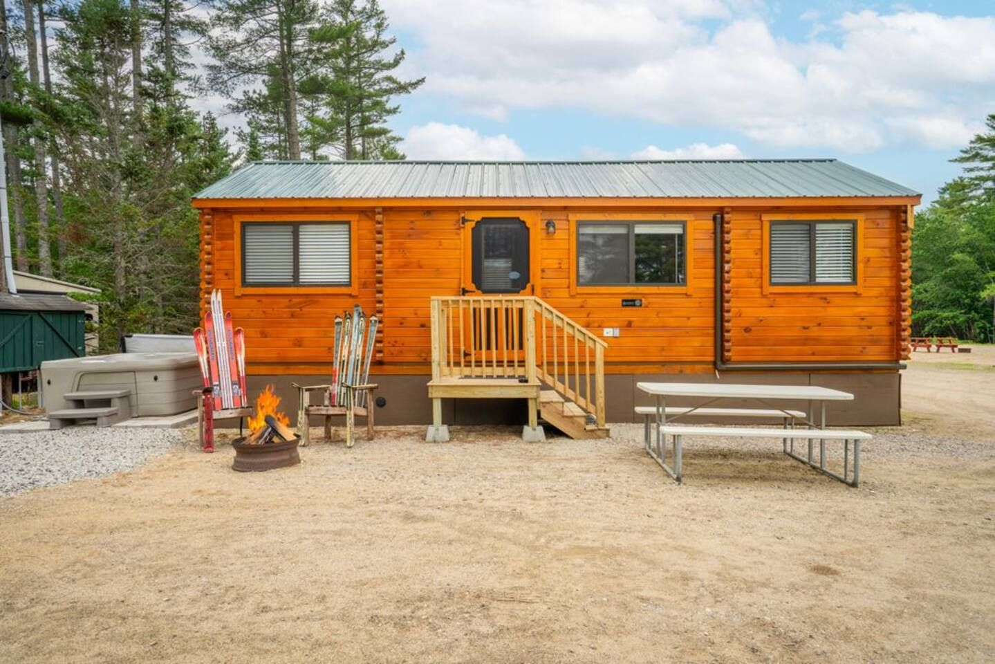 Une cabane avec une façade en bois, un toit en métal, un porche à l’avant avec un banc et un foyer extérieur.