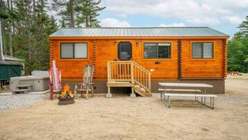 Une cabane avec une façade en bois, un toit en métal, un porche à l’avant avec un banc et un foyer extérieur.