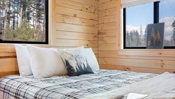 Une chambre dans un chalet en bois, avec un lit, des oreillers et une fenêtre donnant sur la forêt.