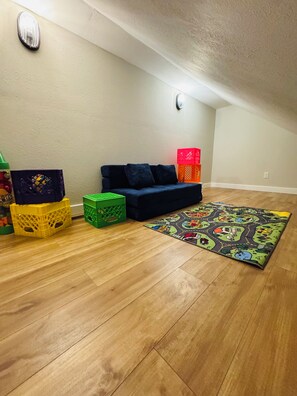 Ein Zimmer mit Holzboden, einem dunkelblauen Sofa, bunten Aufbewahrungsboxen und einem gemusterten Teppich.