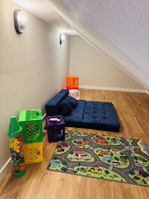 Ein Eckzimmer mit einem blauen Sofa, bunten Spielmatten und Aufbewahrungsboxen.