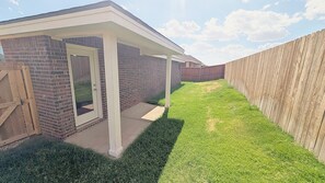 A backyard with a brick house, a wooden fence, and a covered patio area. - Quiet Midland Family Home (Midland)