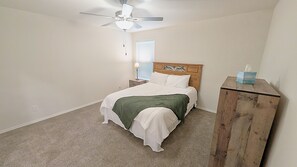 A bedroom with a bed, a nightstand, a wooden dresser, a ceiling fan, and a window with blinds. - Quiet Midland Family Home (Midland)