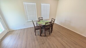 A dining area with a wooden table and chairs, two windows with blinds, and a light-colored floor. - Quiet Midland Family Home (Midland)