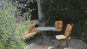Eine Außenpatio mit einem runden Tisch und zwei Stühlen, umgeben von Kübelpflanzen und einem kleinen Baum.