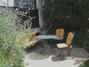 Eine Außenpatio mit einem runden Tisch und zwei Stühlen, umgeben von Kübelpflanzen und einem kleinen Baum.
