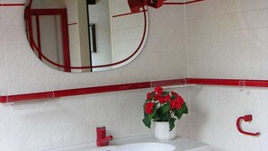 Ein Badezimmer mit einem weißen Waschbecken, einem roten Wasserhahn und einem topfgefäß mit einer roten Blume.