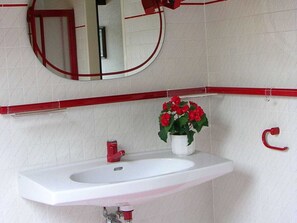 Ein Badezimmer mit einem weißen Waschbecken, einem roten Wasserhahn und einem topfgefäß mit einer roten Blume.