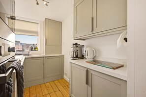 Eine kleine Küche mit Fenster, einer Kaffeemaschine und einem Wasserkocher auf der Arbeitsfläche.