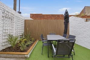 Eine Terrasse mit Tisch und Stühlen, umgeben von einer weißen Ziegelmauer und einem Holzzaun.