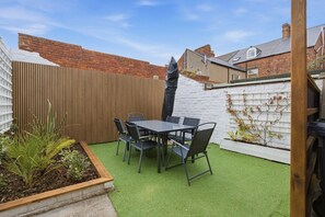 Eine Terrasse mit Tisch und Stühlen, umgeben von einem Holzzaun und einer weißen Backsteinmauer.