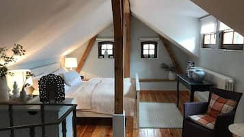 A cozy attic bedroom with a bed, a chair, a table, and a radiator.