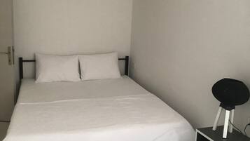 A bedroom with a bed, a bedside table, a lamp, and a window.