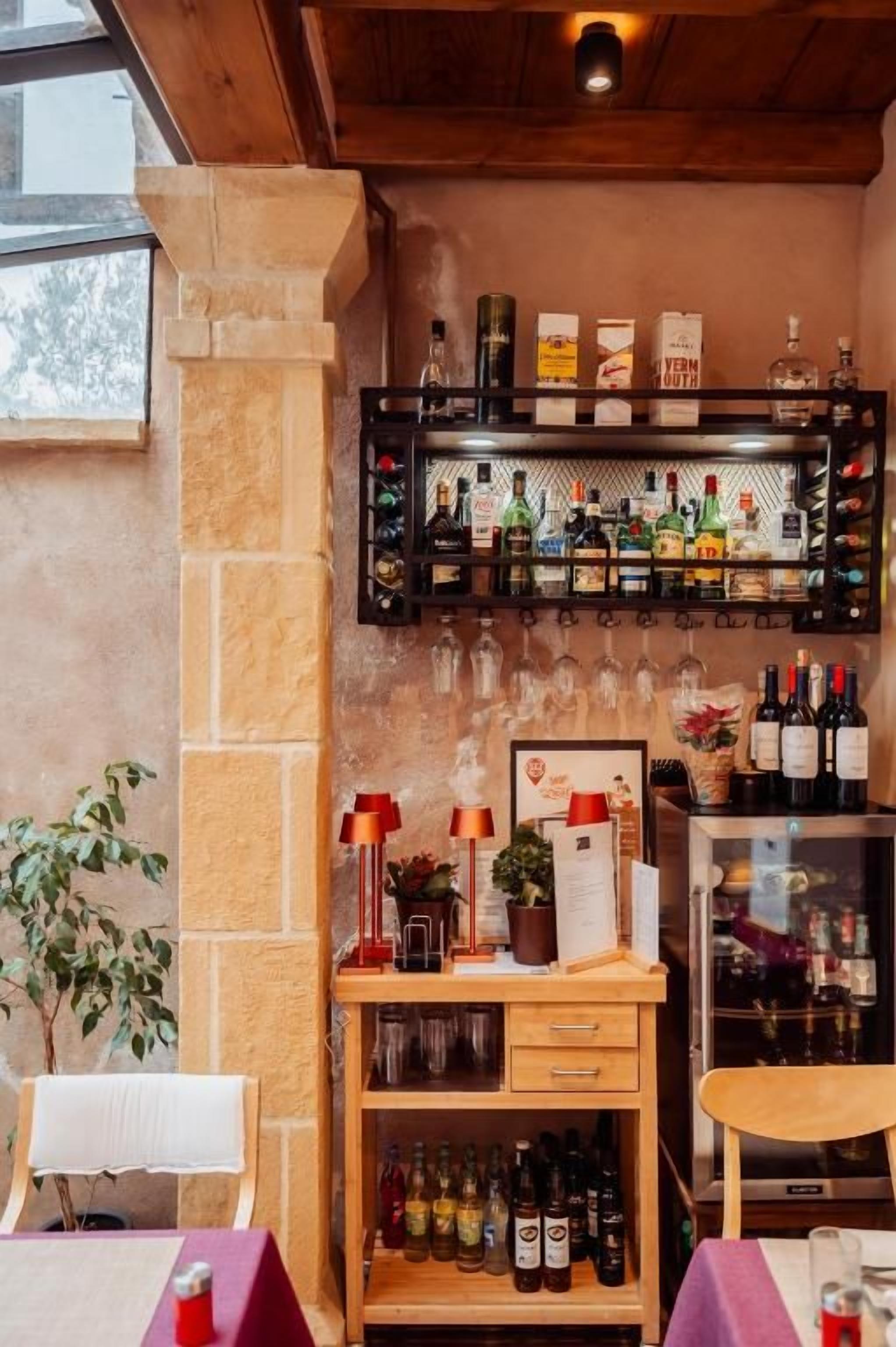 A bar area with shelves of bottles, a wooden counter, and a seating area with a table and chairs.
