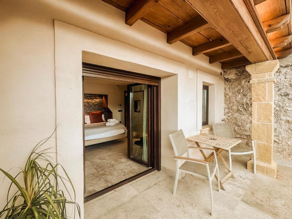 A room with a bed, a table, and chairs, a potted plant, and a stone wall.