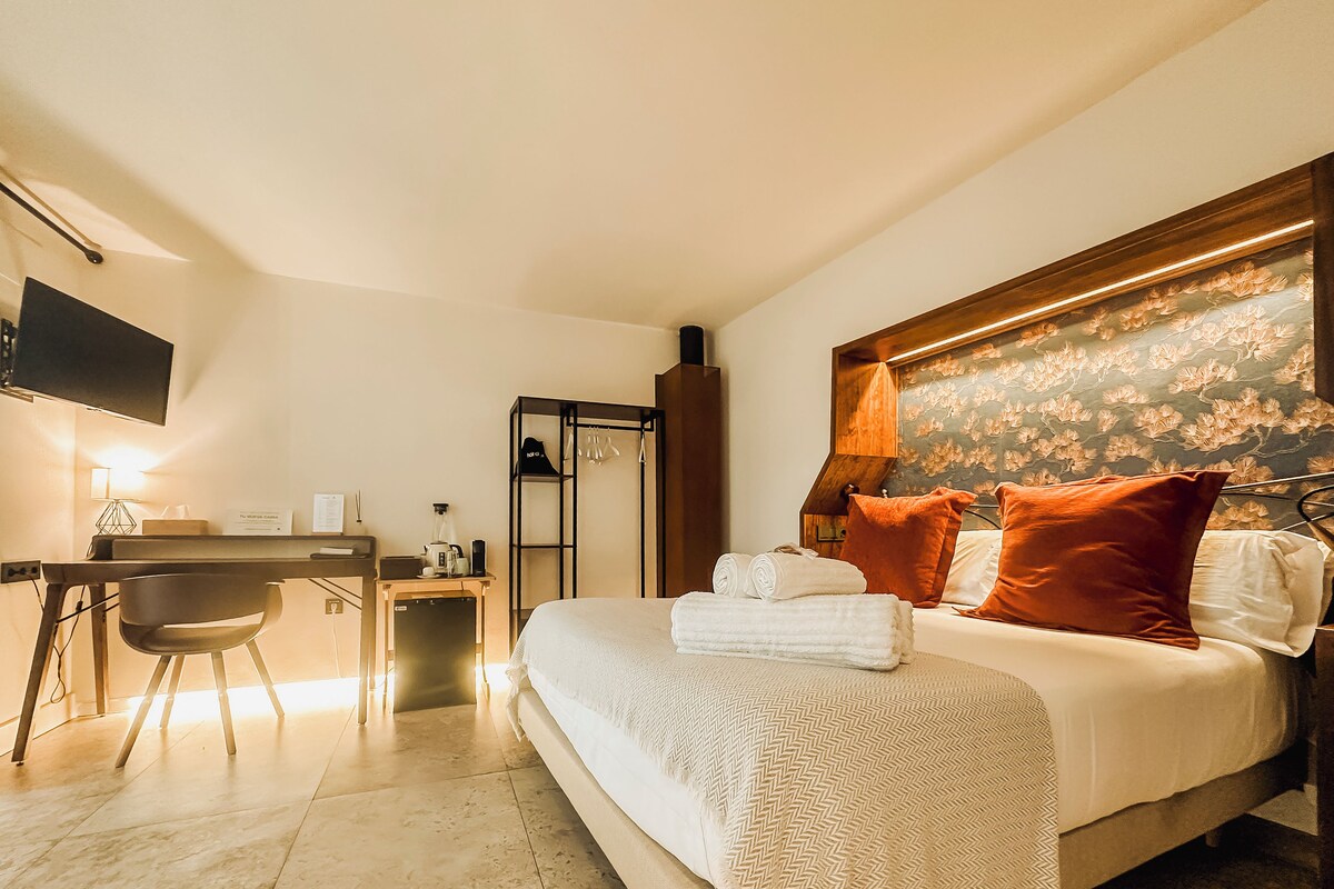 A hotel room with a bed, a desk, a chair, a flat-screen TV, and a mirror.