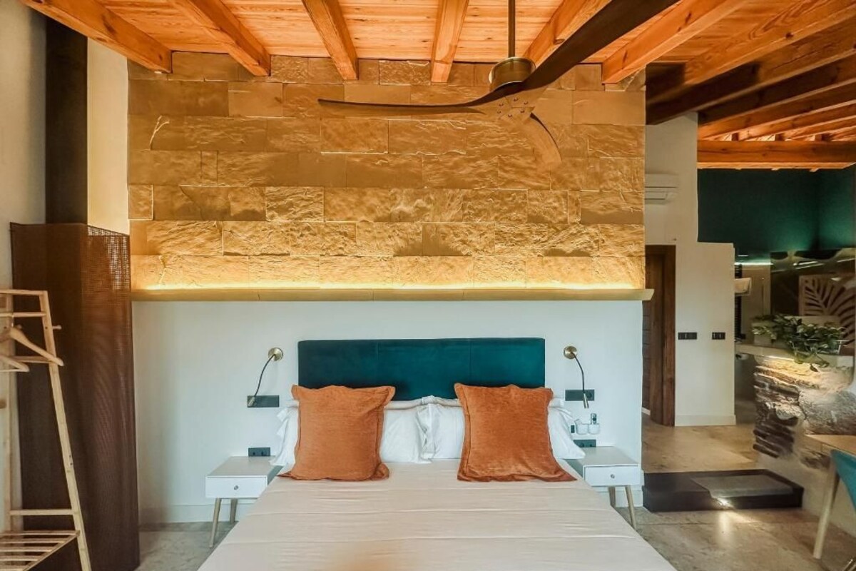 A bedroom with a stone wall, a bed with two pillows, a nightstand, and a wooden ladder.