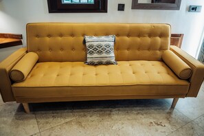 A sofa with a tufted backrest and a decorative pillow, positioned in a room with a tiled floor and wooden elements. - Hotel Poeta Jorge Manrique (Segura de la Sierra)