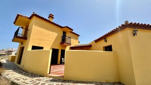 A yellow building with a tiled roof, a balcony, and a stone pathway.