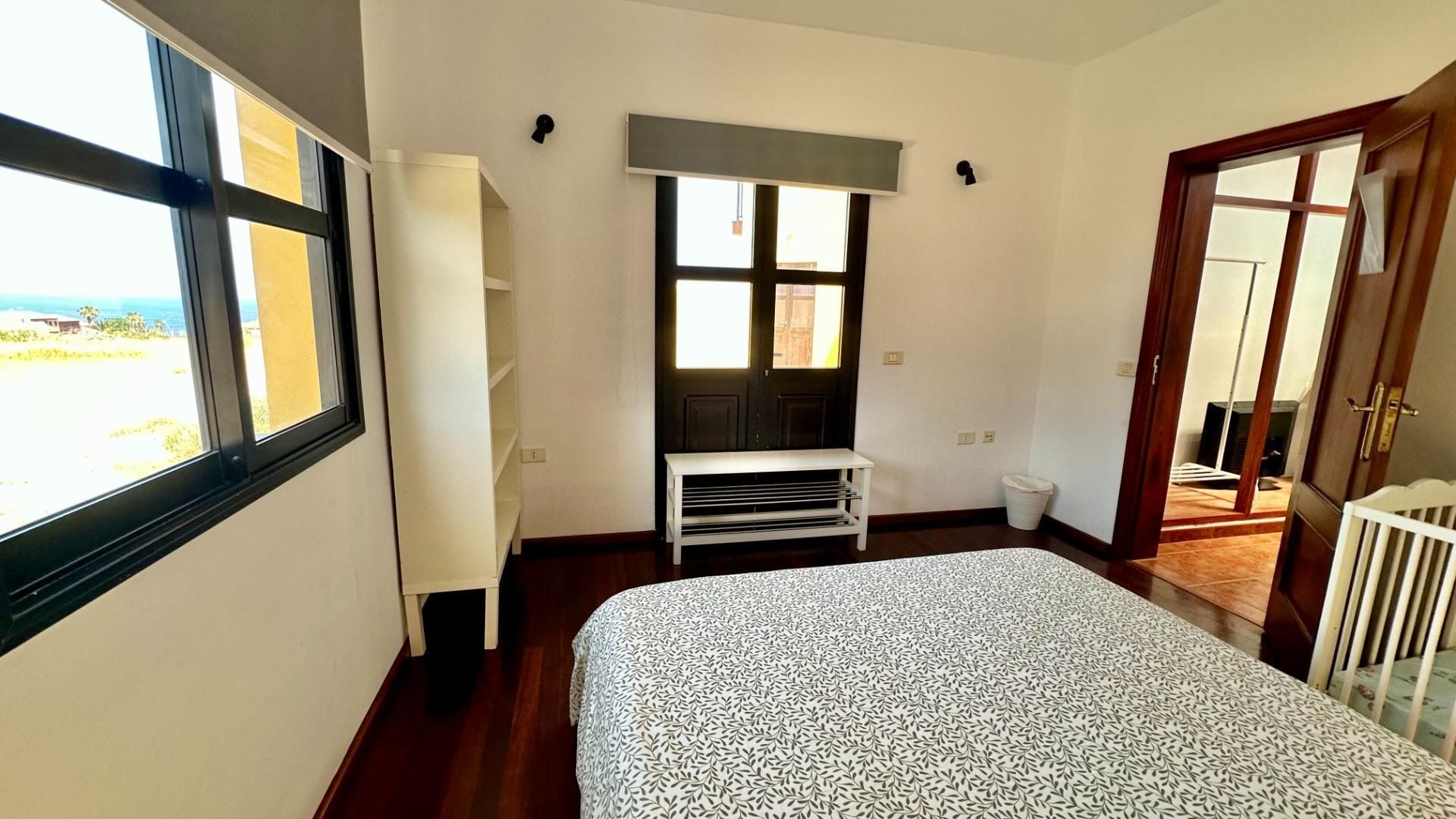 Een slaapkamer met een bed, een raam, een deur en een kleine witte bank.