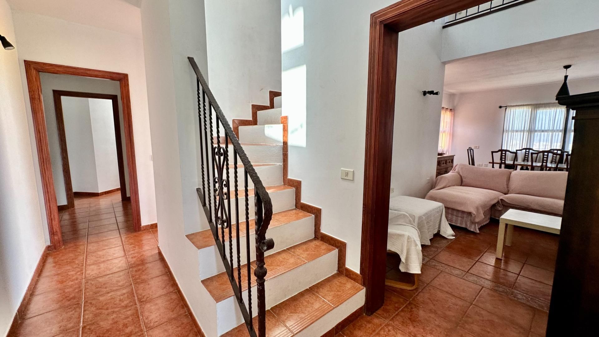 A staircase with a wooden handrail leading to a living area with a sofa and a dining table.