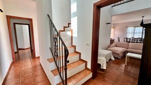 A staircase with a wooden handrail leading to a living area with a sofa and a dining table.