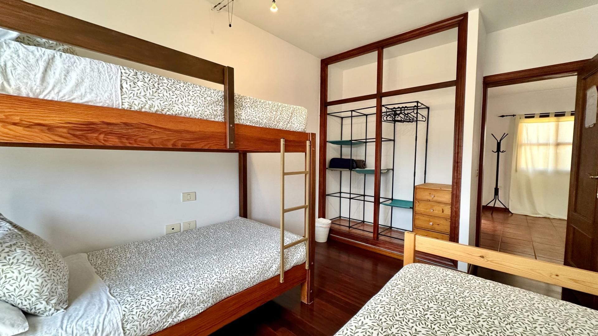A bunk bed with a ladder, a wooden dresser, and a metal shelf unit in a room with wooden flooring and a sliding door.