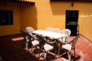 Un patio al aire libre con una mesa y sillas blancas, una parrilla y una pared amarilla.