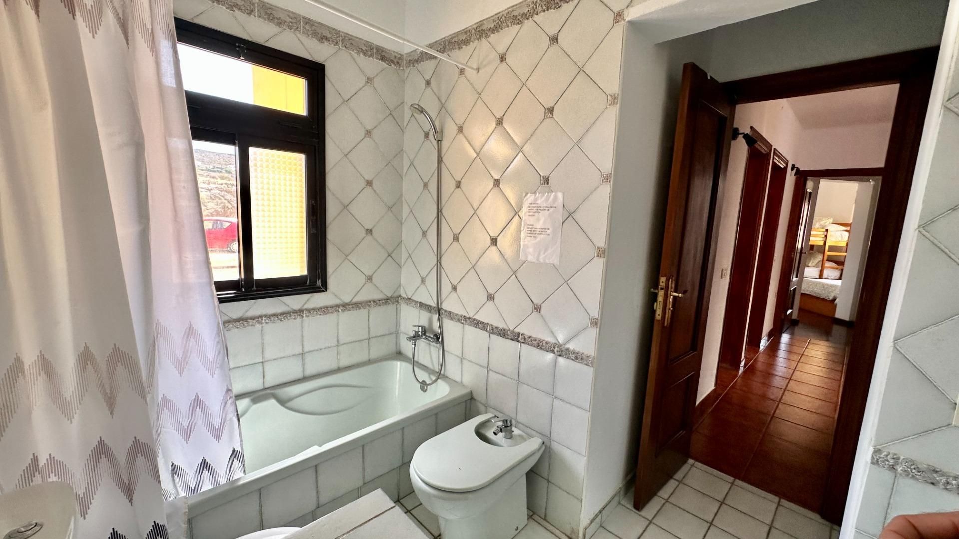 Een badkamer met een bad, toilet en douche. Er is een raam met uitzicht op buiten.