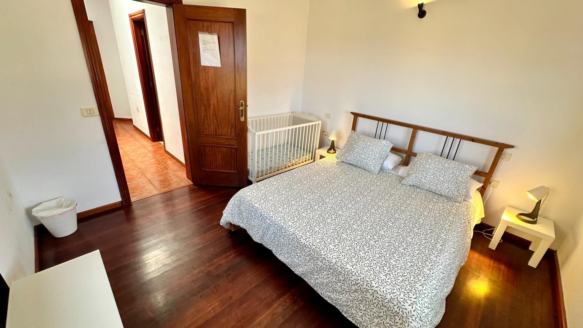 Een slaapkamer met een houten bed, een ledikant en een nachtkastje met een lamp.