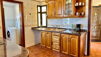 A kitchen with wooden cabinets, a sink, a coffee maker, and a washing machine.