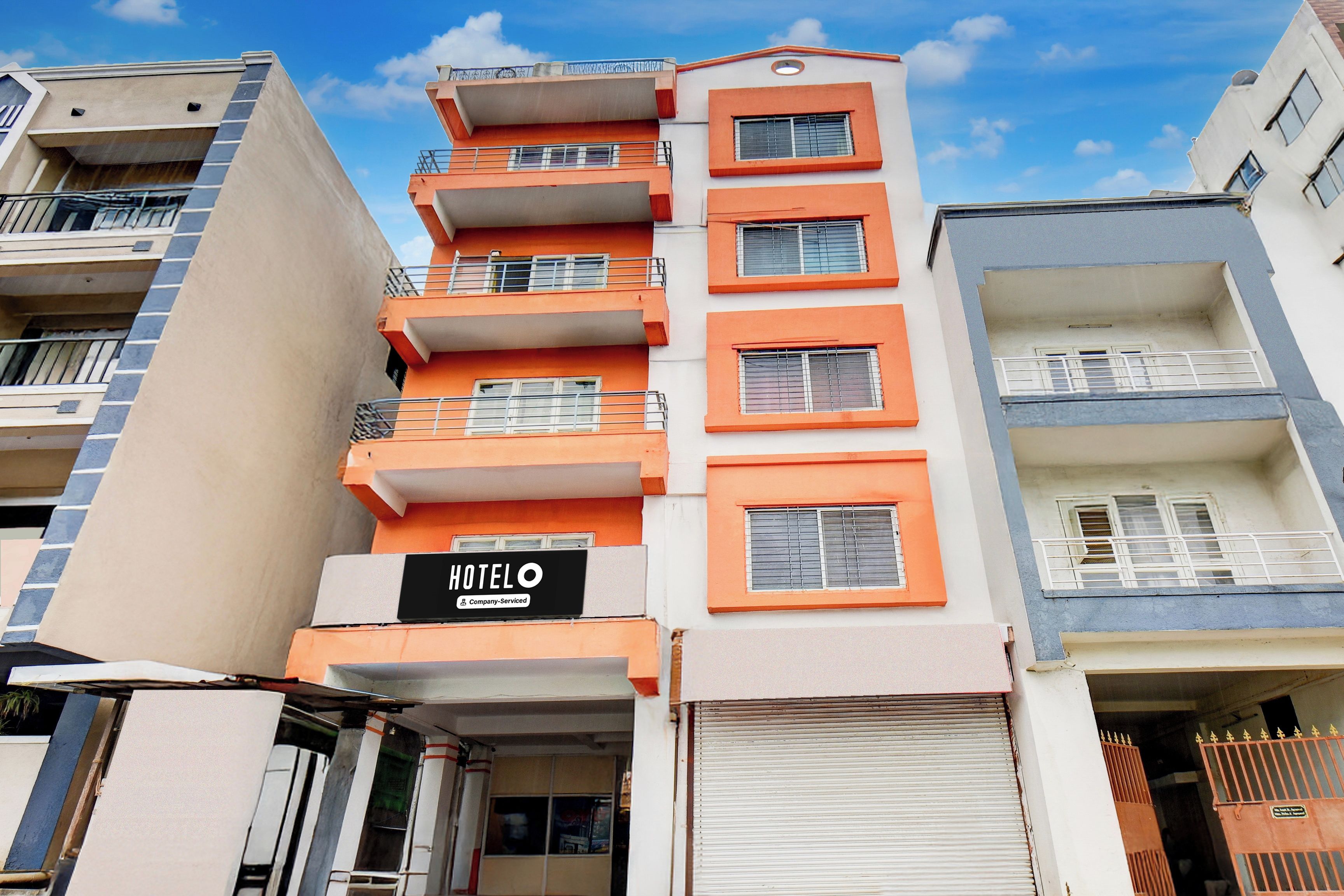 Un hotel de varios pisos con balcones, un cartel que indica que ofrece servicios de empresa y un obturador cerrado en la entrada.