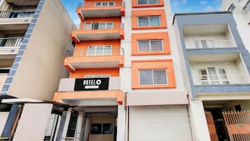 Un hotel de varios pisos con balcones, un cartel que indica que ofrece servicios de empresa y un obturador cerrado en la entrada.