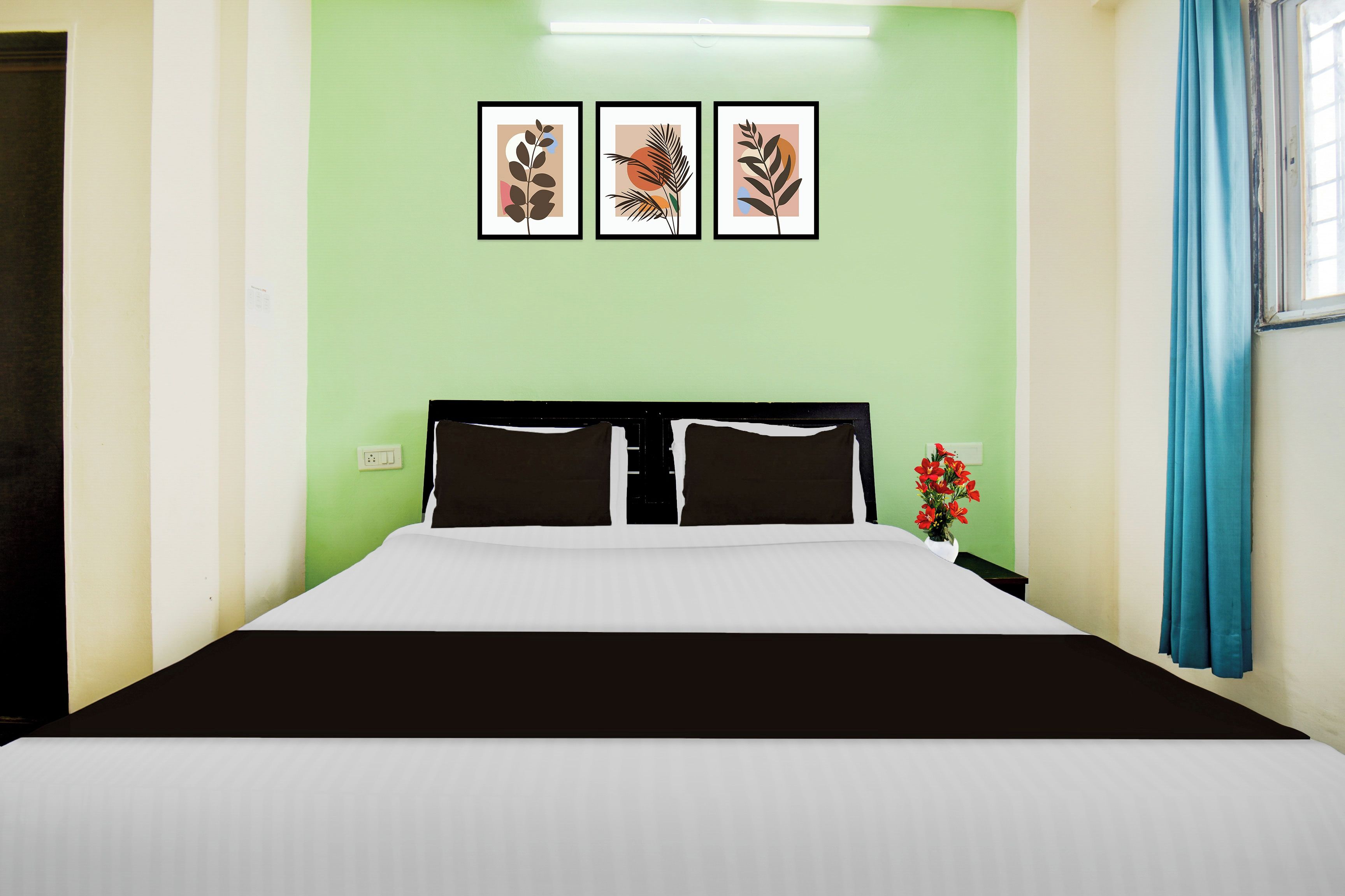 Habitación de hotel con cama, mesita de noche, un jarrón con flores y tres cuadros en la pared.