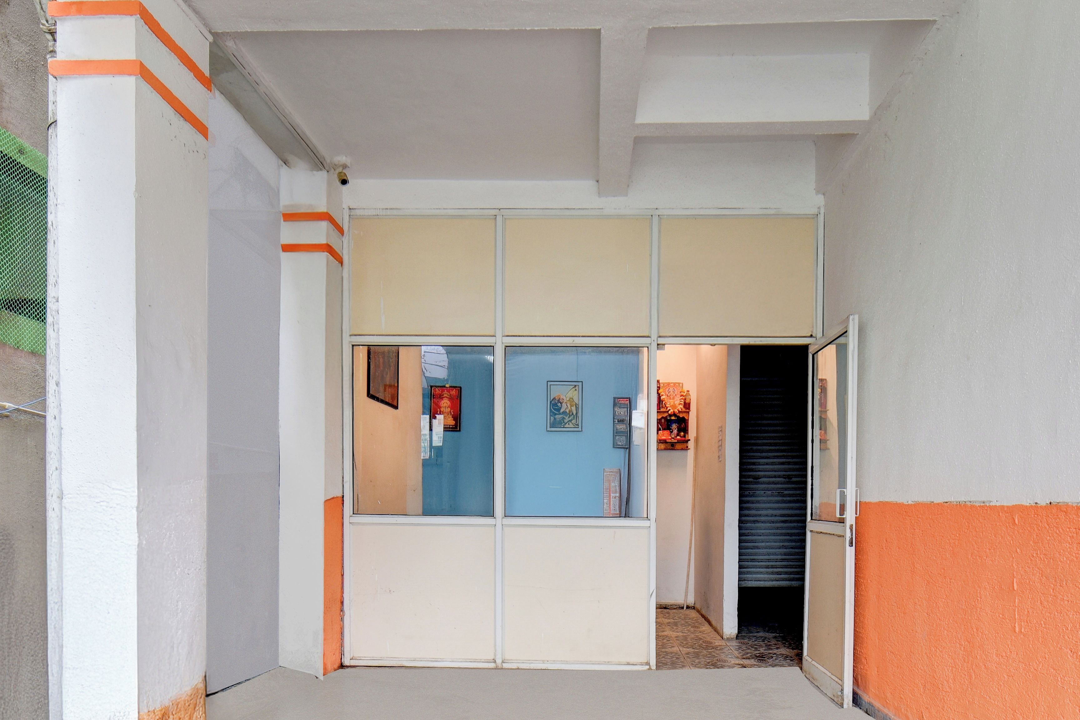 Un pasillo con una puerta azul, paredes blancas y detalles color naranja.