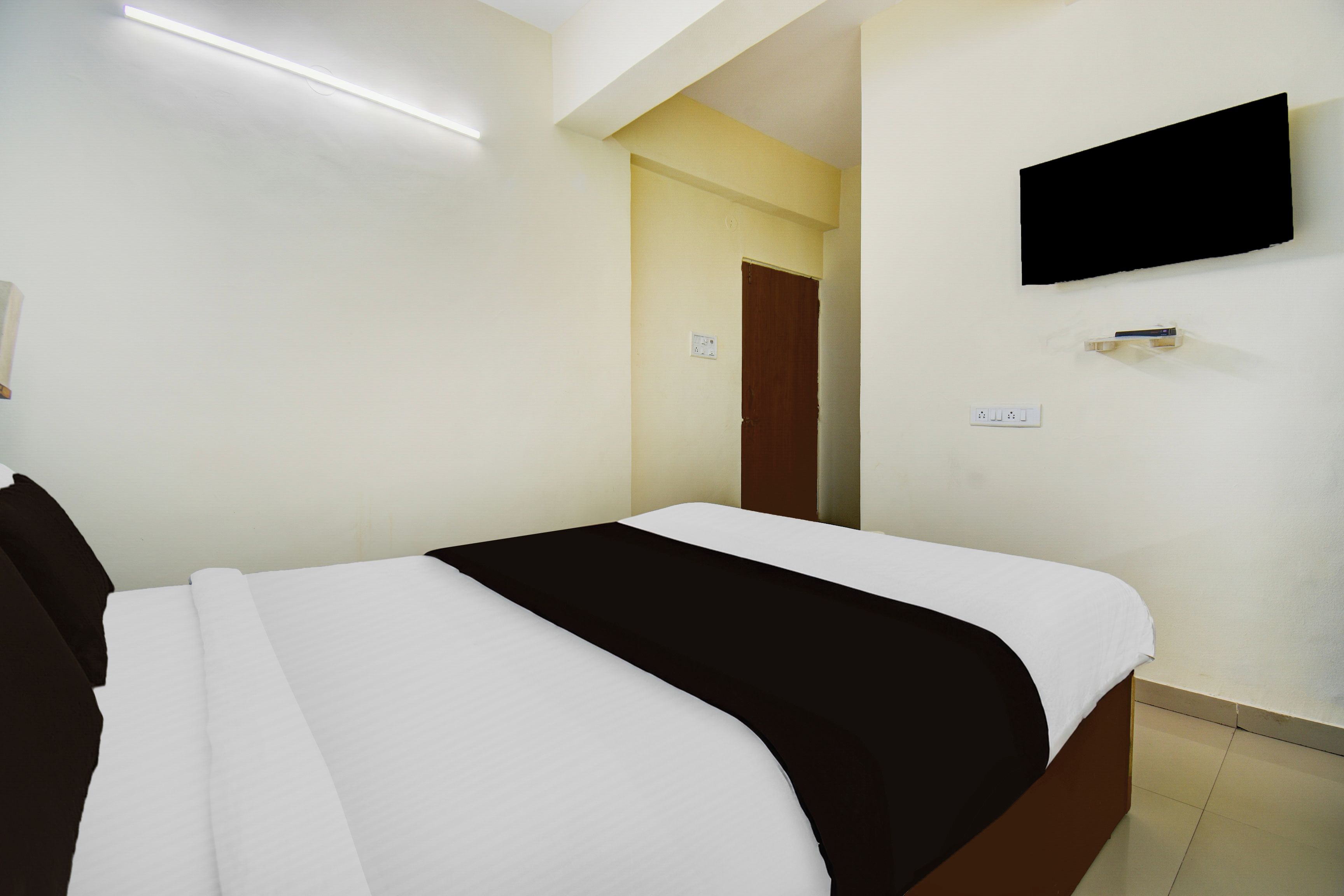Quarto de hotel com cama, televisão fixada na parede e porta que dá para outro cômodo.