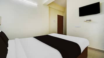 Quarto de hotel com cama, televisão fixada na parede e porta que dá para outro cômodo.